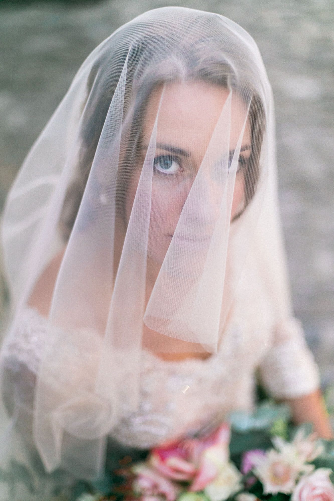 The bride is wearing a veil over her face and holding a bouquet of flowers.