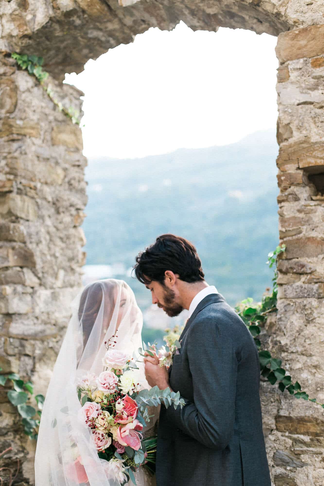 A bride and groom are standing next to each other in front of a stone wall.
