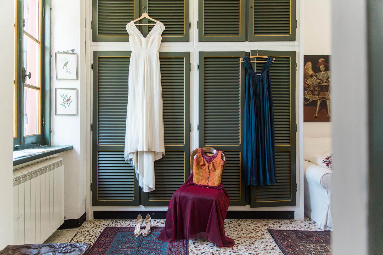A wedding dress is hanging on a hanger in a room next to a chair.