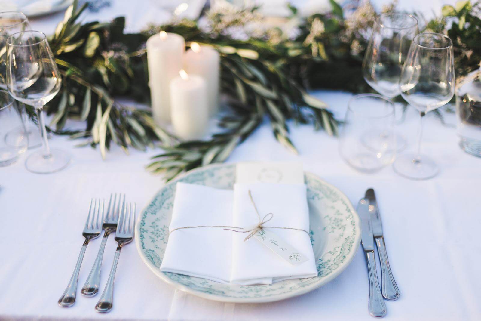 A table setting with plates , forks , knives , candles and wine glasses.