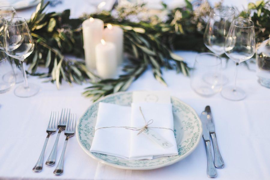 A table set for a wedding reception with plates , forks , knives , and candles.