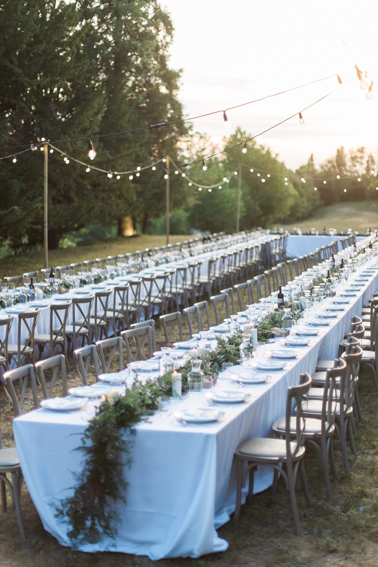 A very long table with a white tablecloth and chairs set up for a wedding reception.
