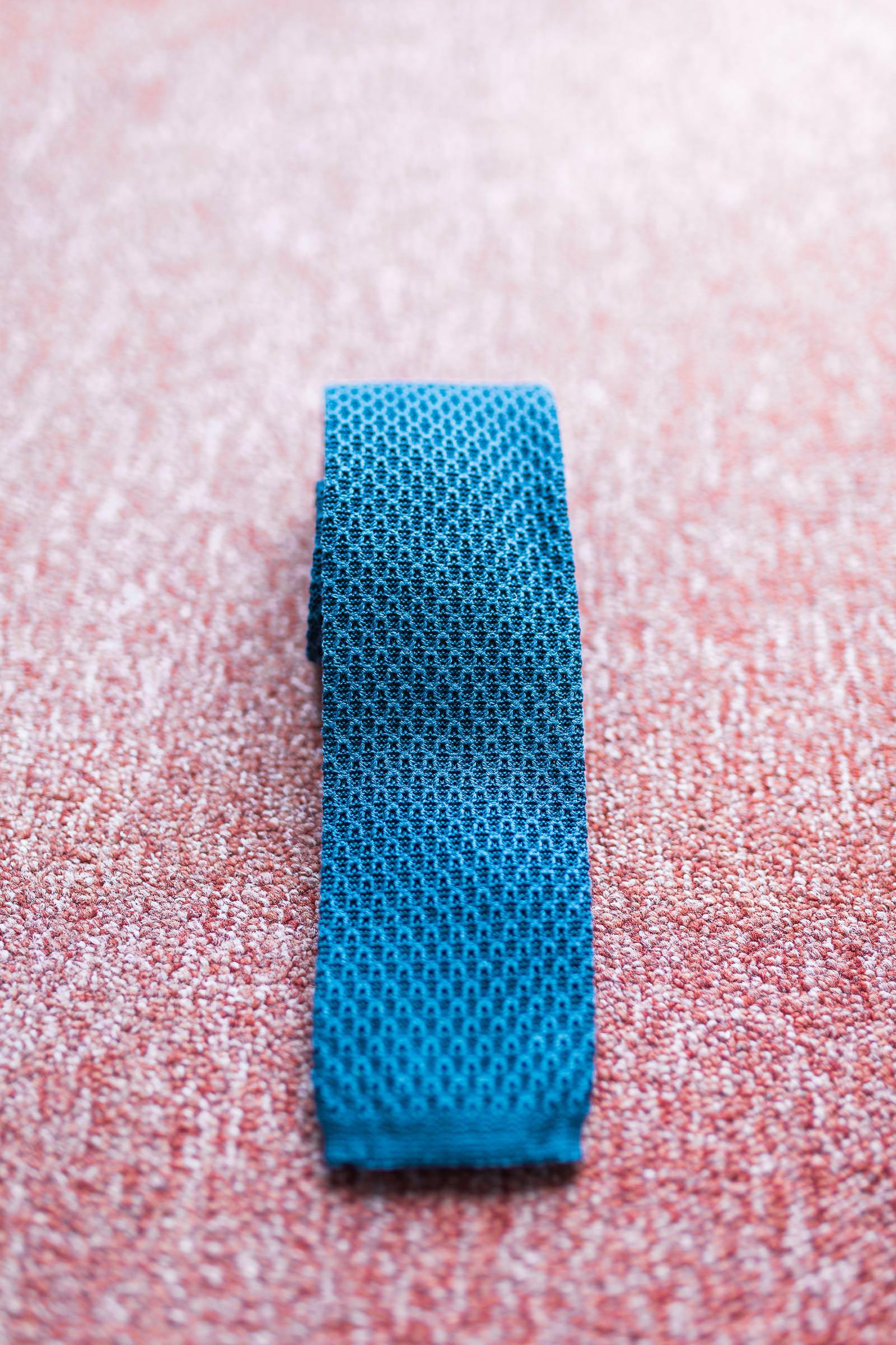 A blue knitted tie is sitting on a pink carpet.