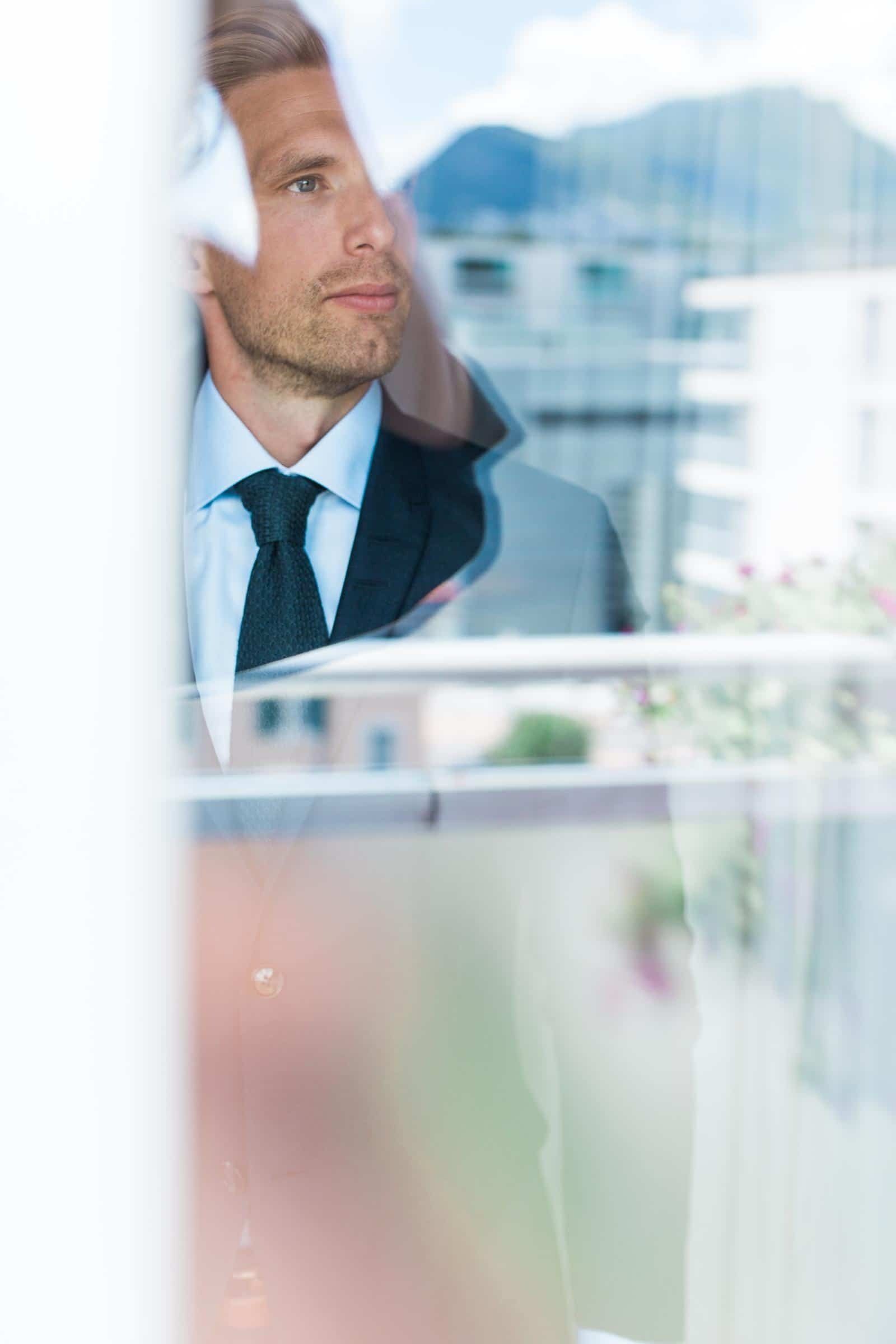 A man in a suit and tie is looking out of a window.