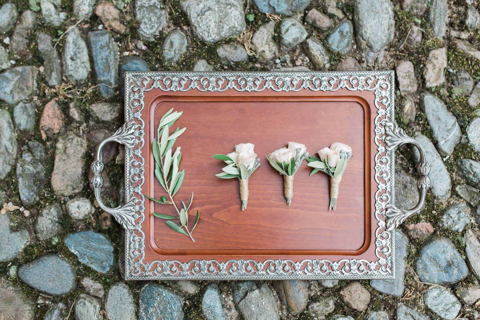 A wooden tray with flowers on it is sitting on a rocky surface.