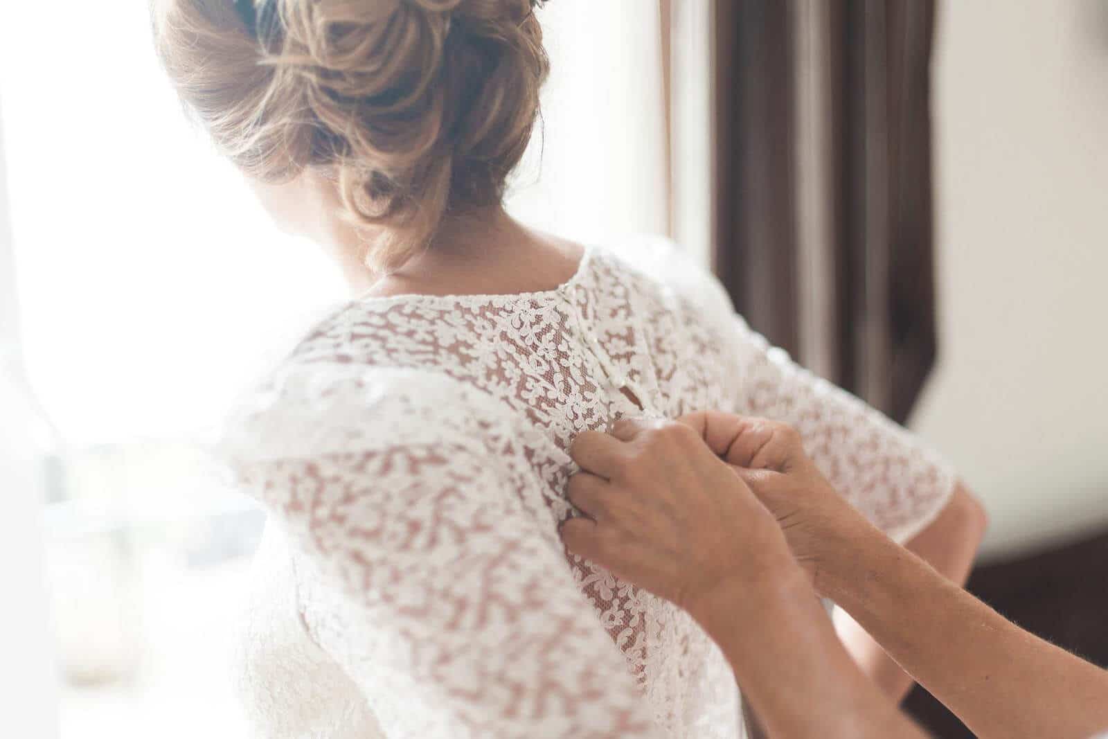 A woman is helping another woman with her wedding dress.