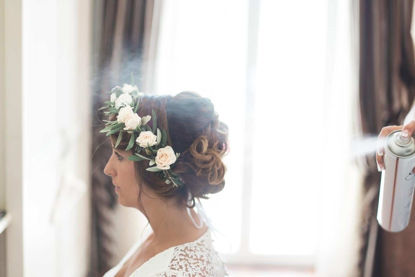 A woman with a flower crown on her head is getting her hair sprayed.