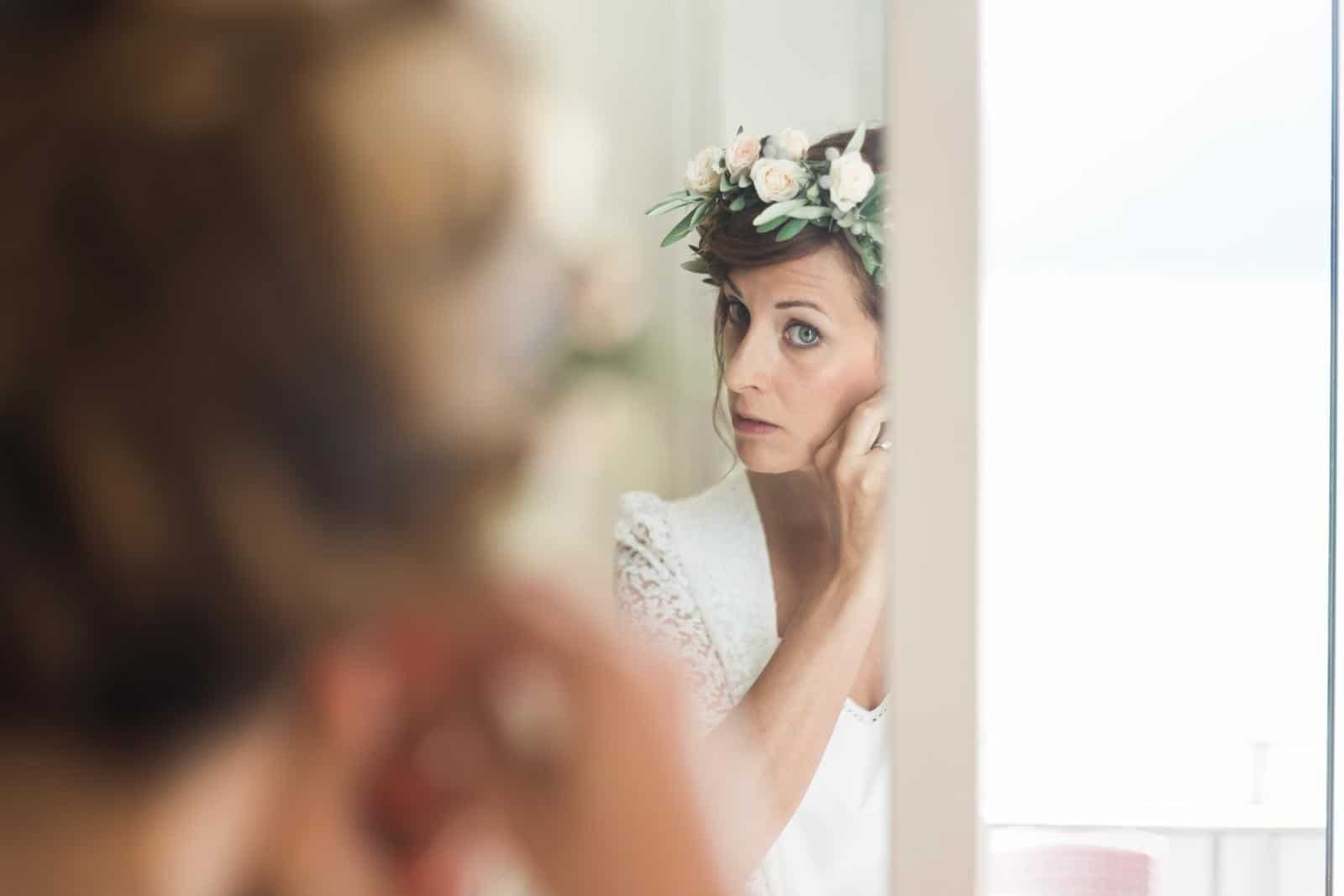 A woman wearing a flower crown is looking at herself in the mirror.