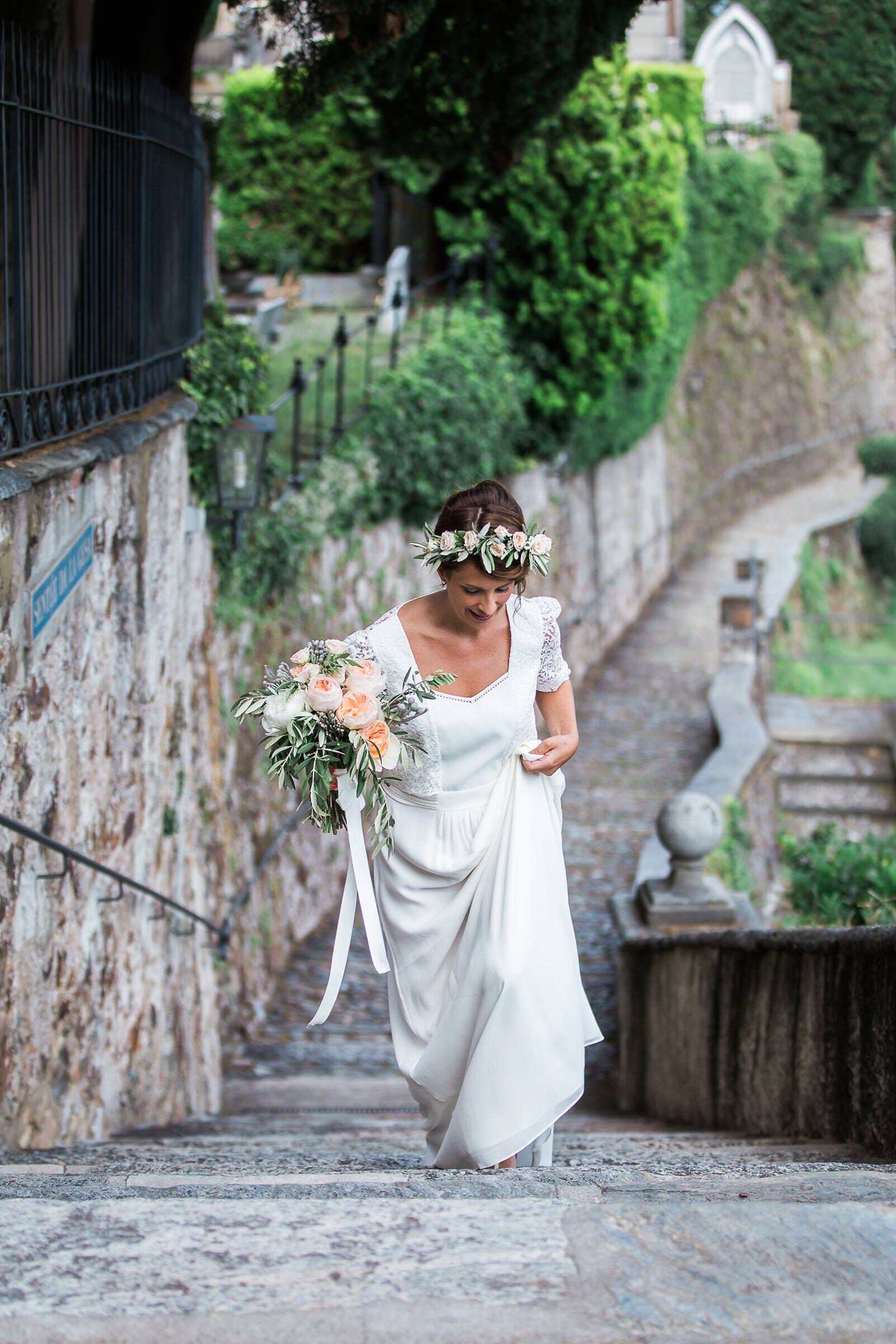A bride in a wedding dress is walking down a set of stairs holding a bouquet of flowers.