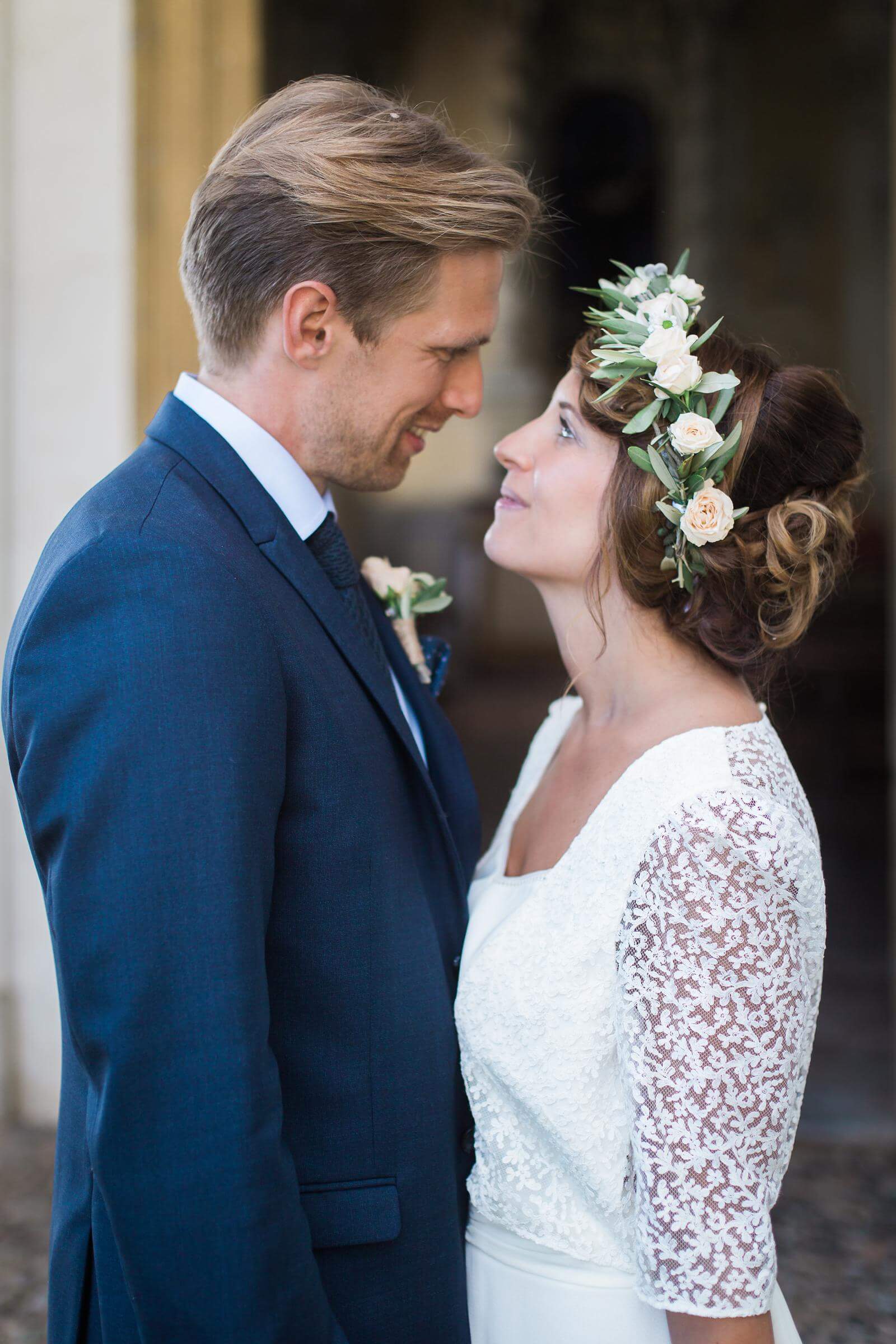 A bride and groom are looking at each other and the bride is wearing a flower crown.