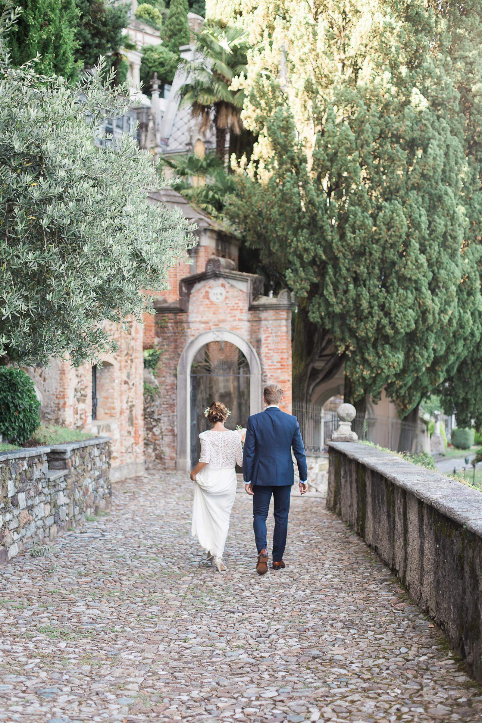 A bride and groom are walking down a cobblestone path.