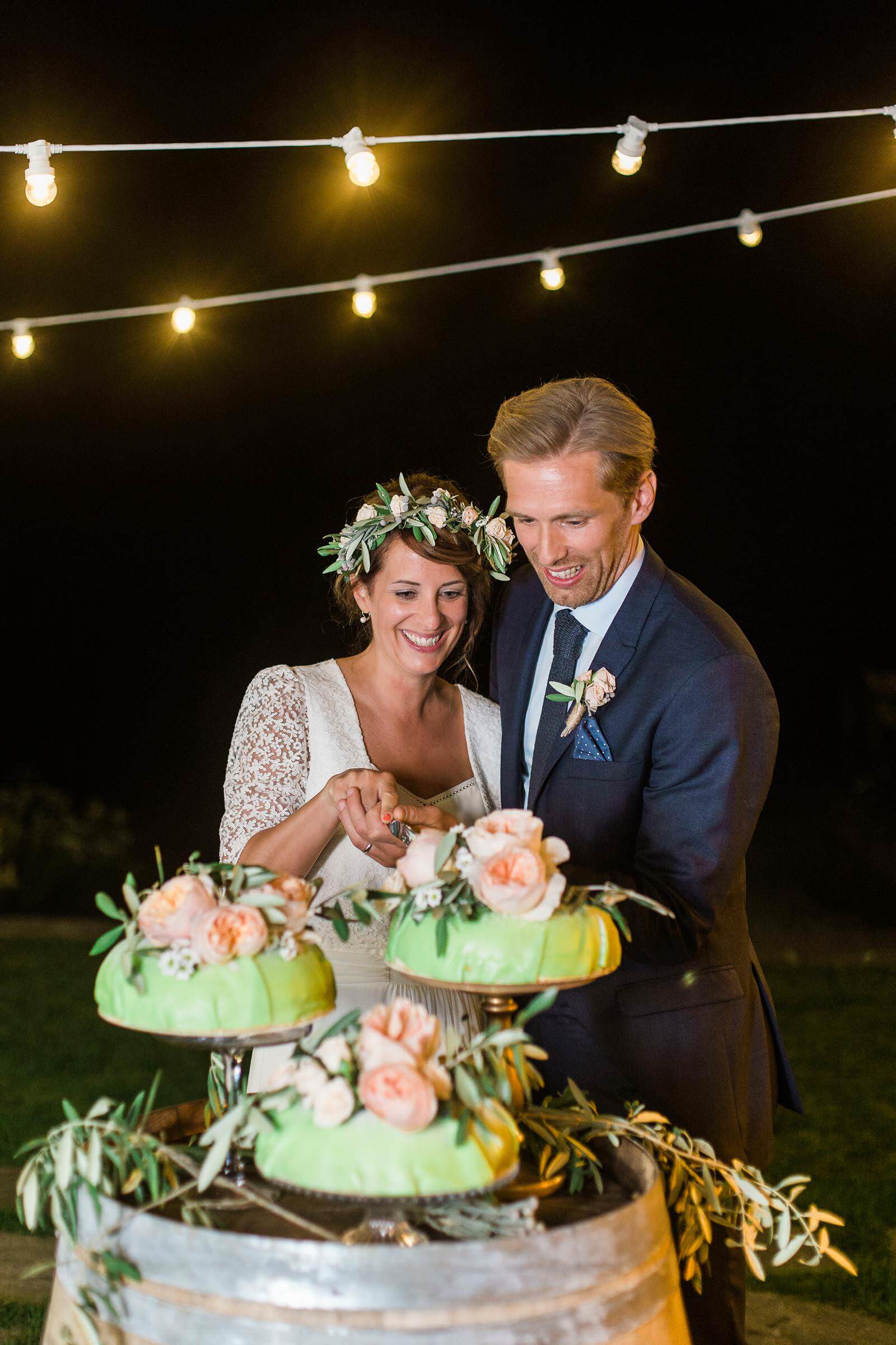 A bride and groom are cutting their wedding cake at night.