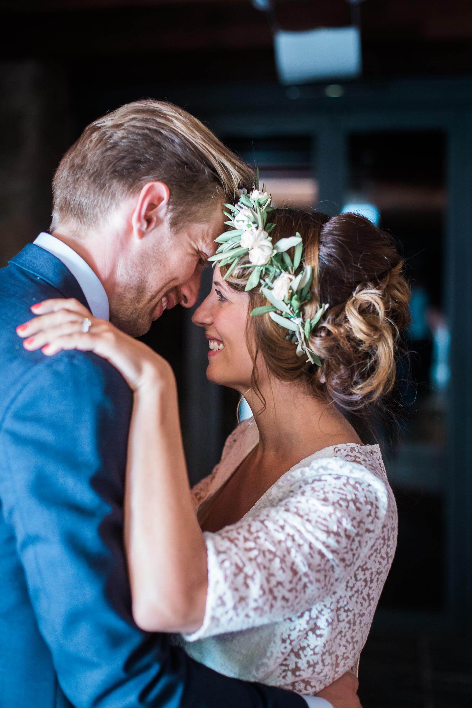 A bride and groom are dancing at their wedding and the bride is wearing a flower crown.