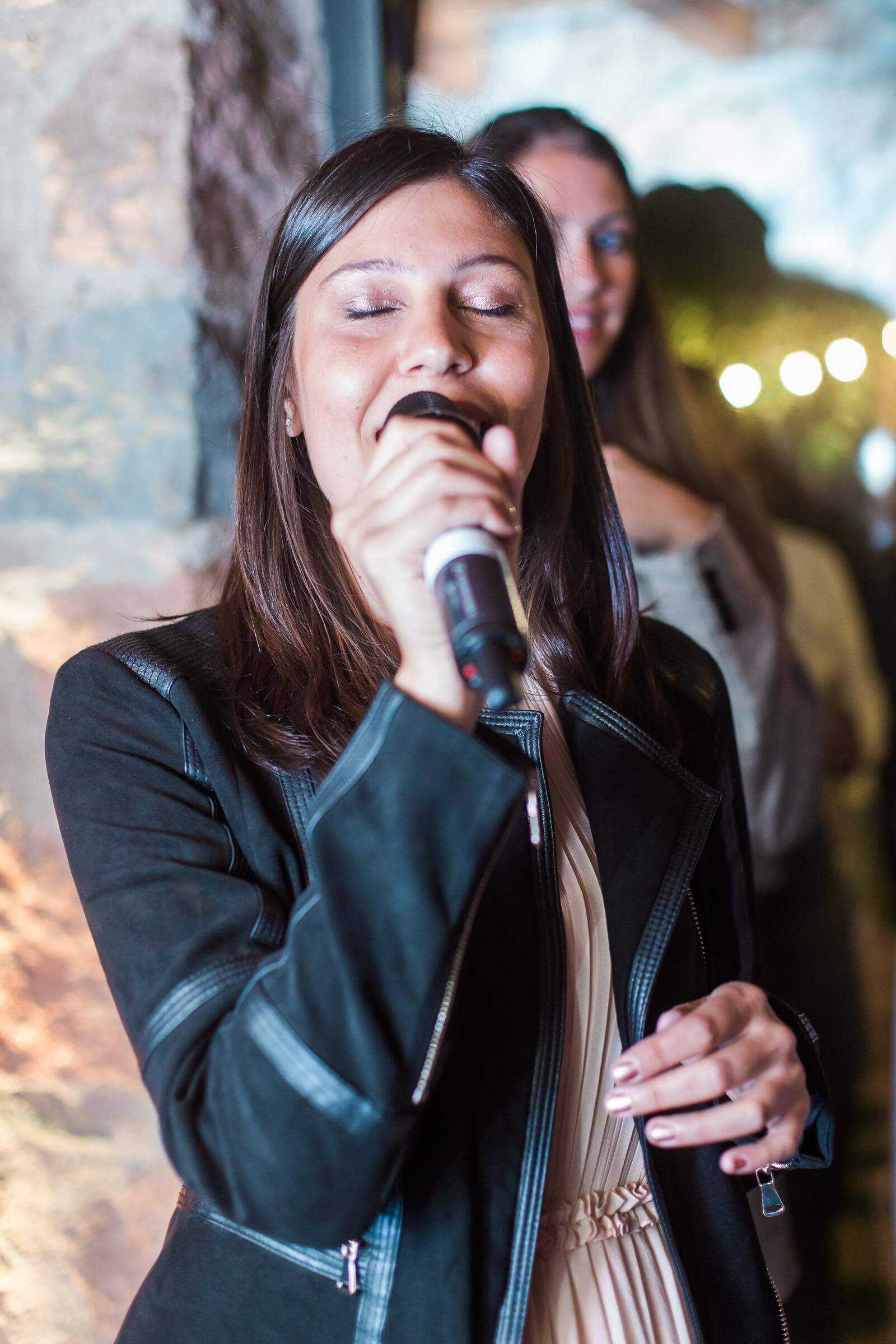A woman in a black jacket is singing into a microphone.