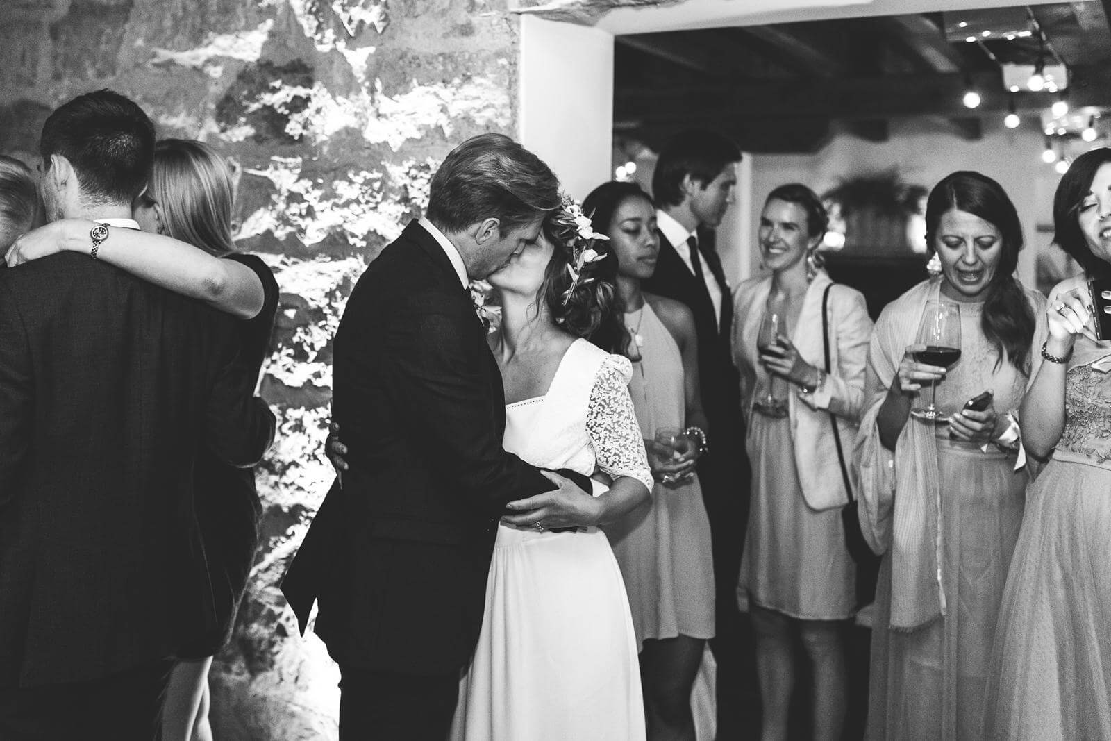 A black and white photo of a bride and groom kissing at a wedding reception.
