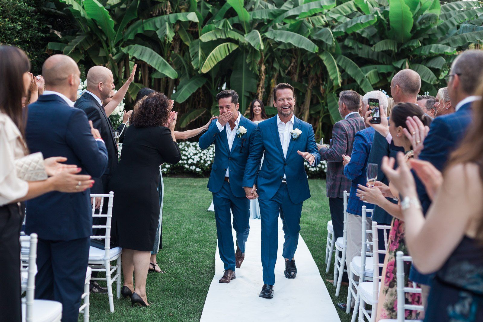 Two men in suits are walking down the aisle at a wedding ceremony.