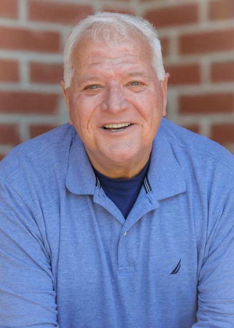 Smiling man in a light blue shirt standing before a brick wall