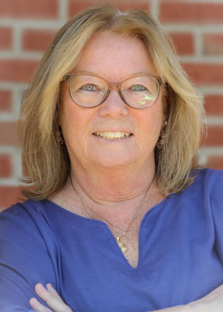 Smiling woman in blue shirt and glasses standing before a brick wall
