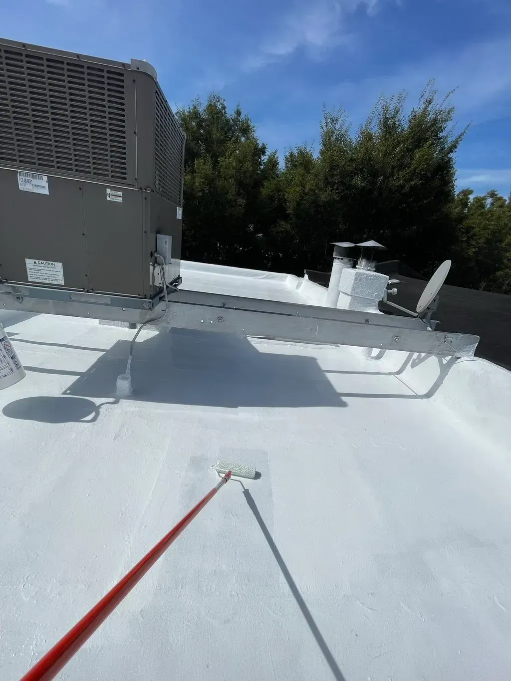 A person is painting a white roof with a roller.