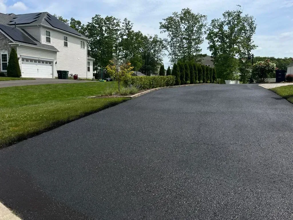 Residential driveway with fresh black asphalt beside a white house and green trees
