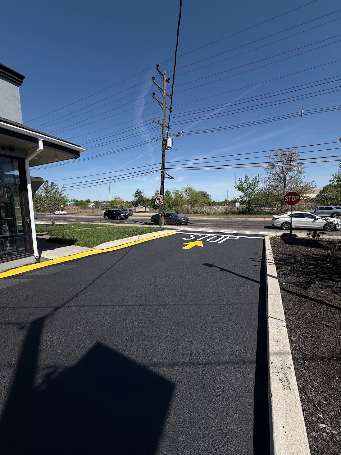 Parking lot driveway with speed bump, stop sign, utility pole, and clear blue sky.