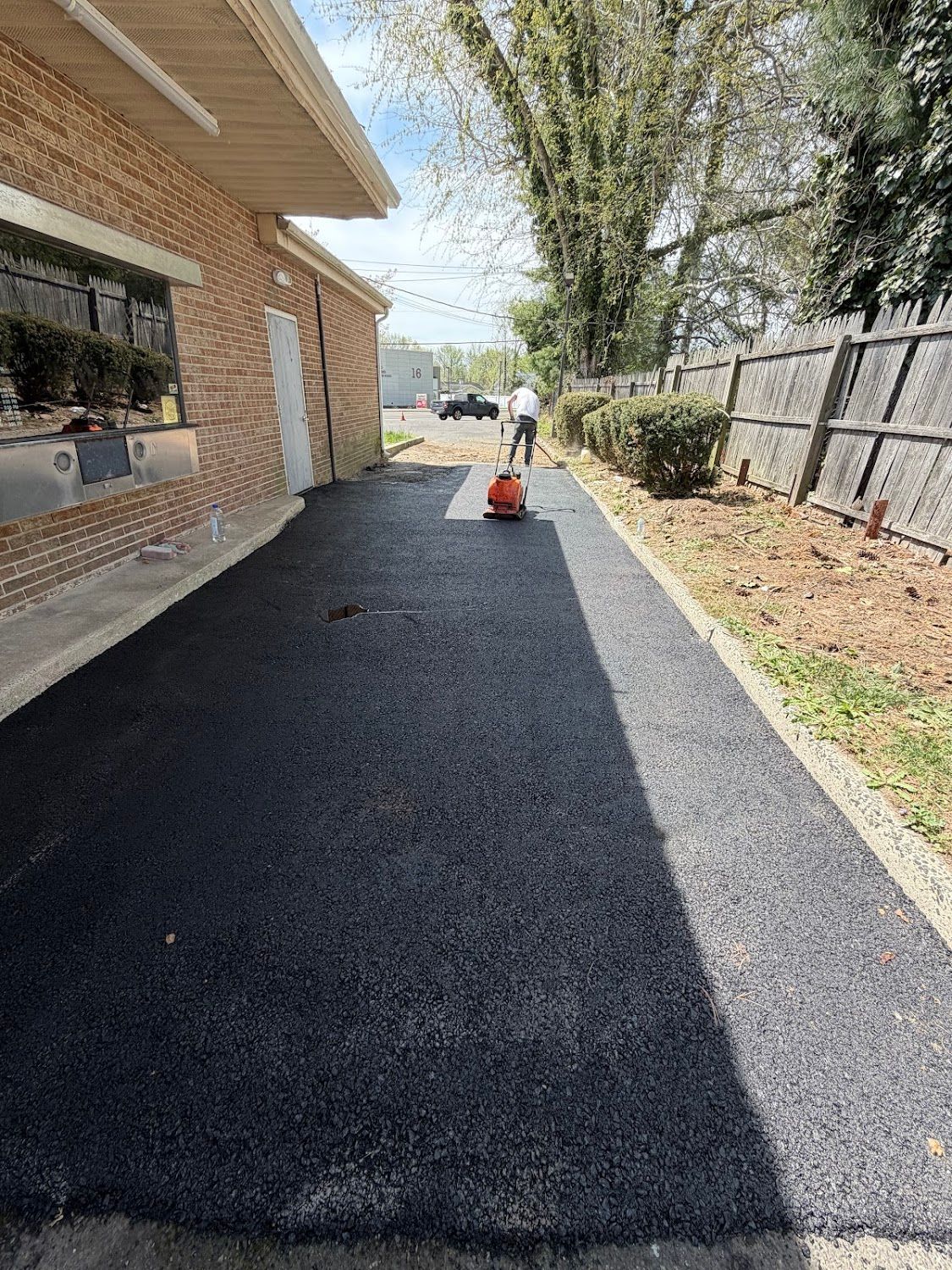 Person using a red leaf blower on a newly paved driveway beside a brick house