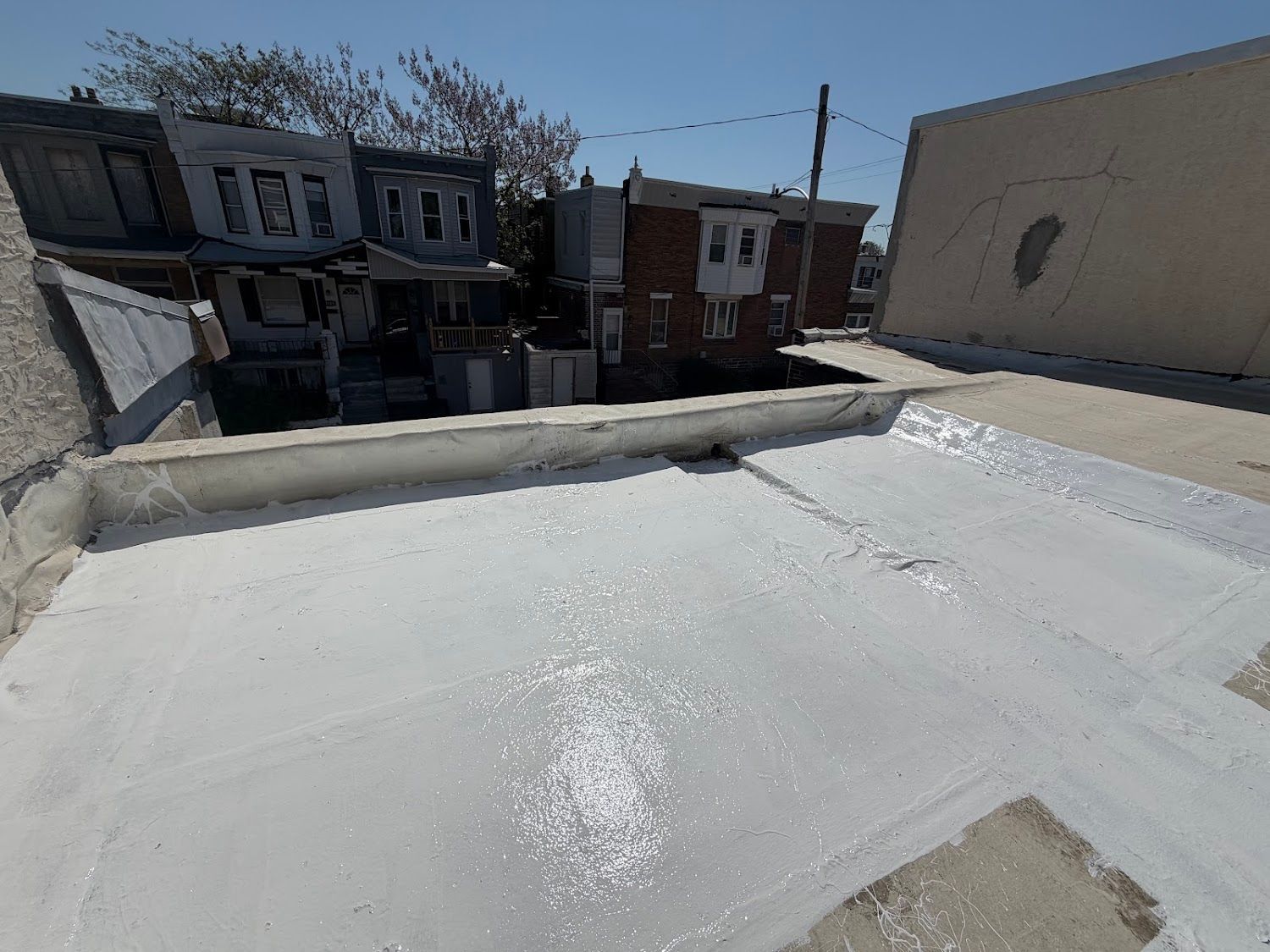 Rooftop covered in white reflective coating beside rowhouses under a clear blue sky.