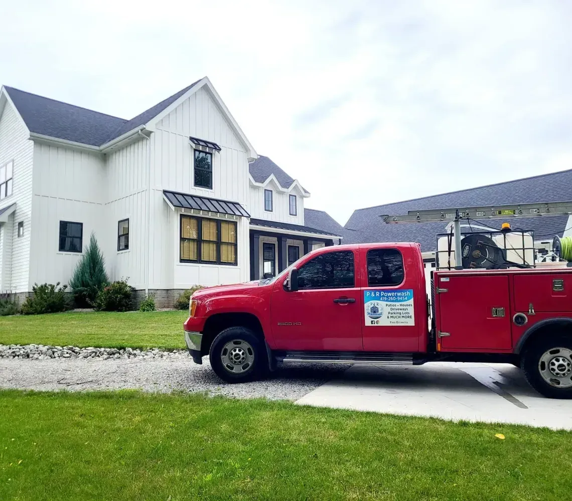 Red utility truck parked outside a white house with a steep roof on a gravel driveway.