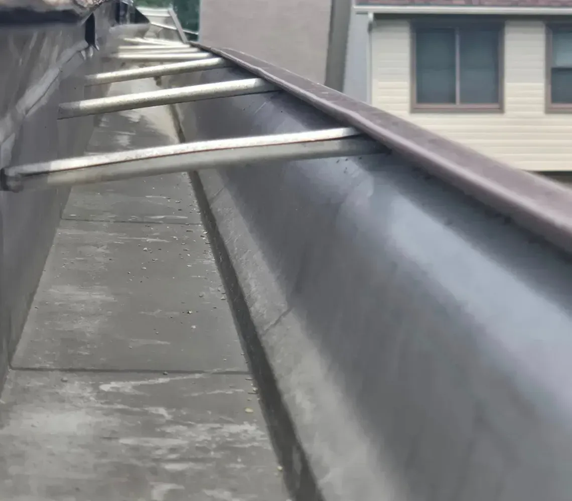 Rooftop gutter line with metal supports beside house roofs on a cloudy day