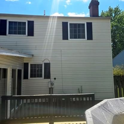 Backyard view of a beige two-story house with black shutters, chimney, and a wooden deck railing.