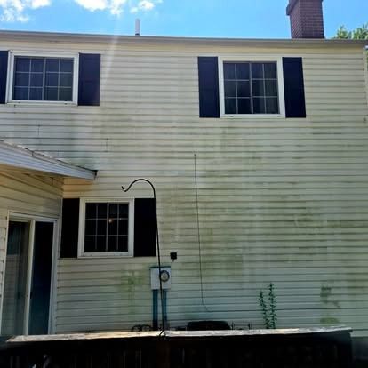 Two-story beige house with black shutters and a small front porch beneath a blue sky