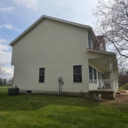 Side view of a beige two-story house with white porch railing and a grassy yard.