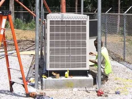 A man is kneeling down next to a large air conditioner.