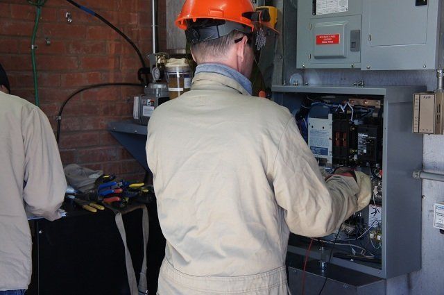 A man wearing a hard hat is working on an electrical box