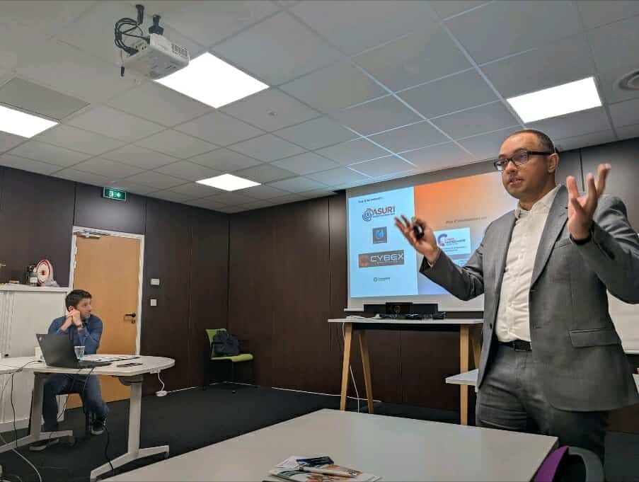 Un présentateur prend la parole dans une salle de conférence tandis qu'une diapositive est projetée sur l'écran.