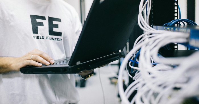 Un technicien travaille sur un ordinateur portable dans une salle serveur, entouré de câbles.