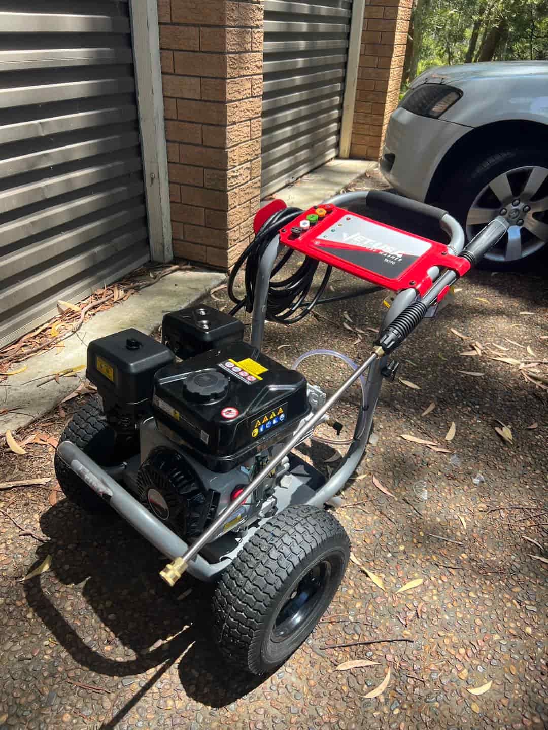 A Pressure Washer Is Parked In Front Of A Garage Next To A Car — Gibbo’s Lawns & Property Maintenance In Salamander Bay, NSW
