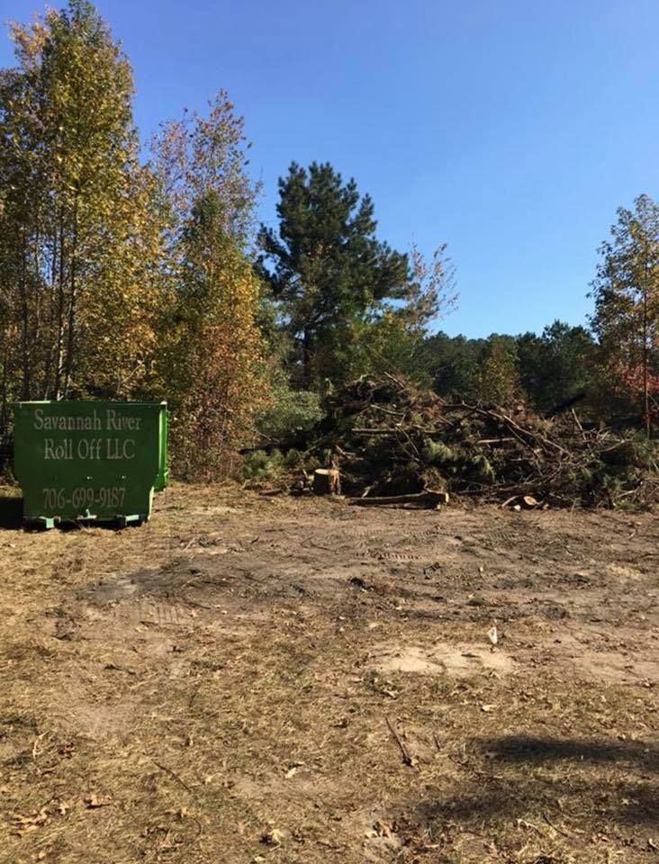 A green dumpster is sitting in the middle of a dirt field.