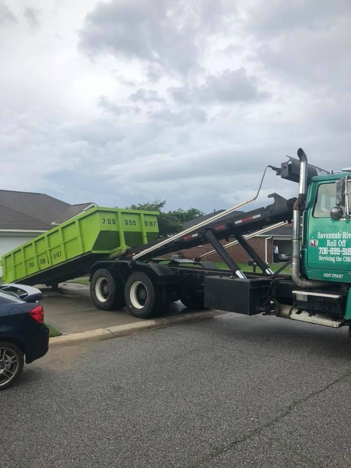 A green dumpster is being towed by a green dump truck.