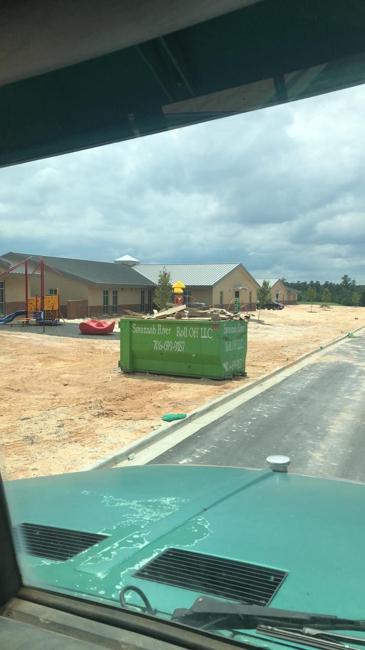 A green dumpster is sitting on the side of the road in front of a building under construction.