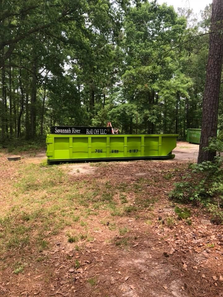 A green dumpster is sitting in the middle of a forest.
