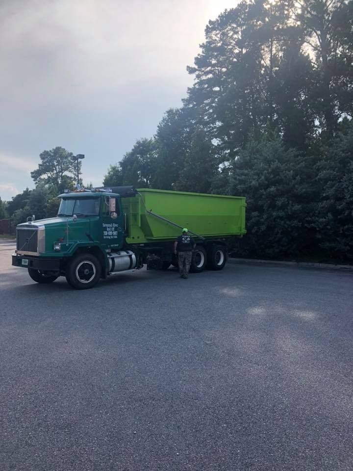 A man is standing next to a green dump truck in a parking lot.