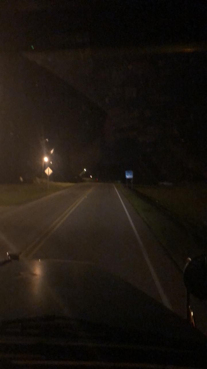 A car is driving down a dark highway at night.