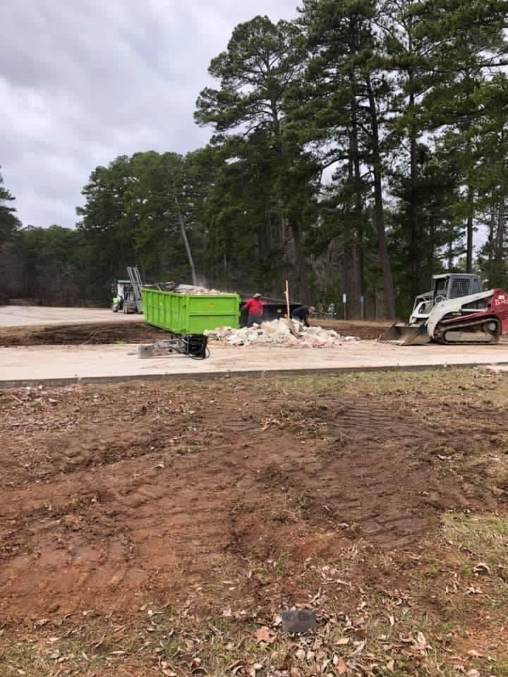 A green dumpster is sitting in the middle of a dirt field.