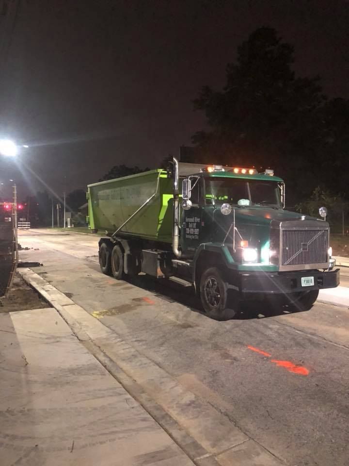 A dump truck is driving down a street at night.