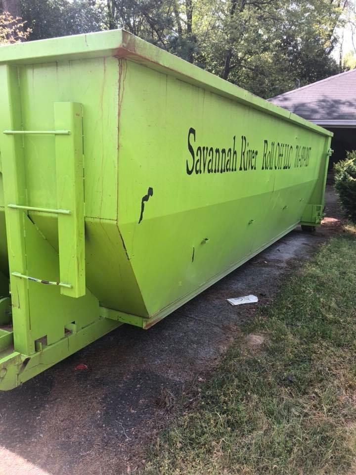 A large green dumpster is parked in a driveway next to a house.