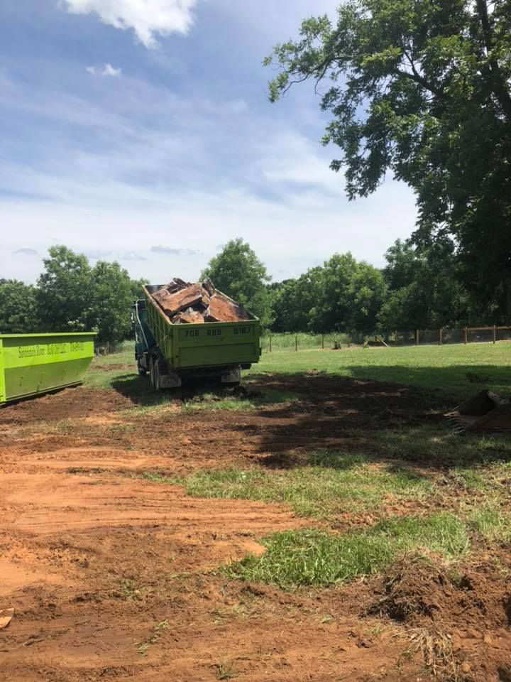 A green dump truck is driving down a dirt road.