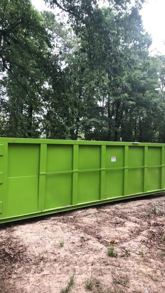 A large green dumpster is sitting in the middle of a dirt field.