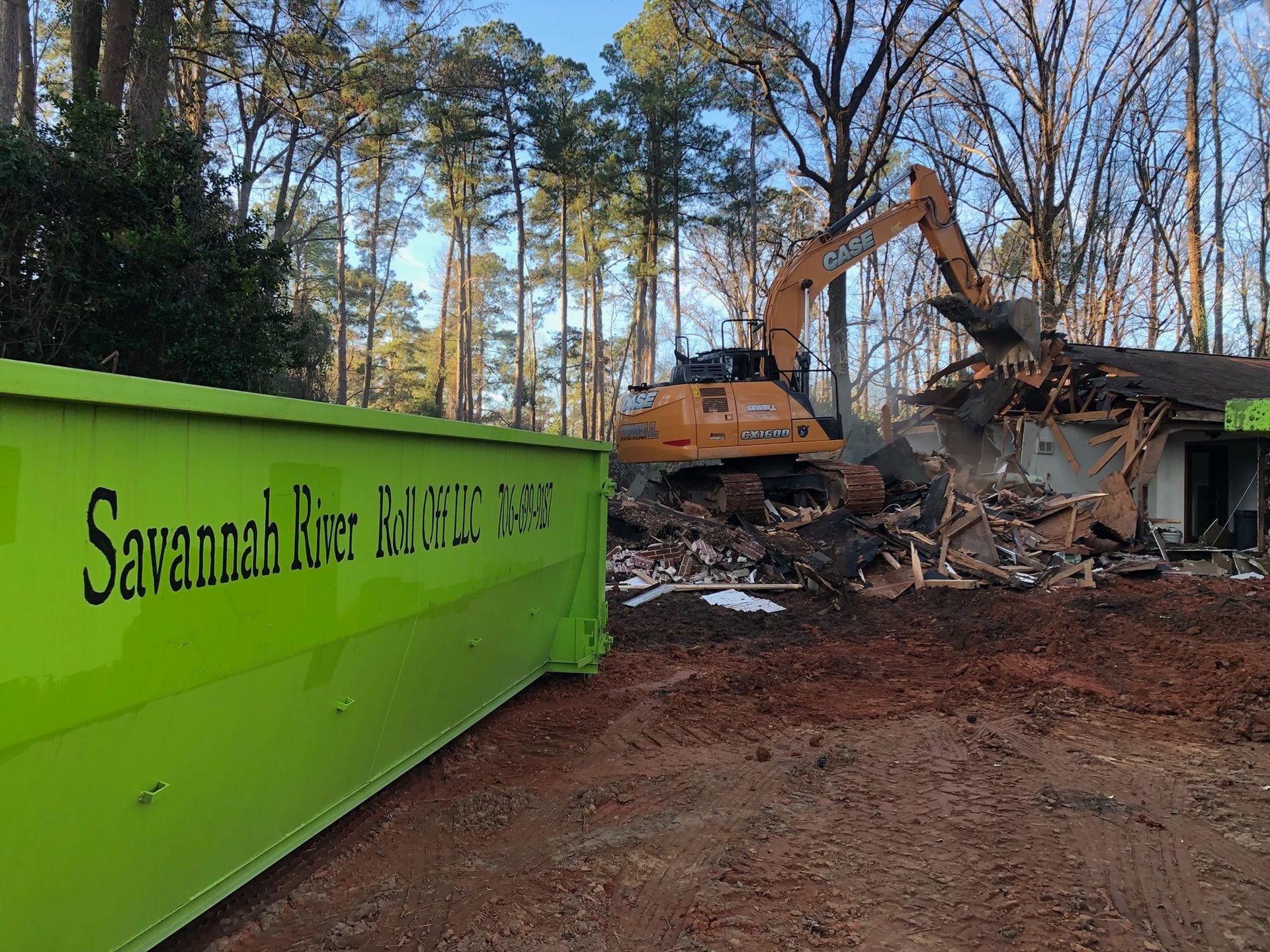 A green dumpster is sitting in front of a house being demolished.