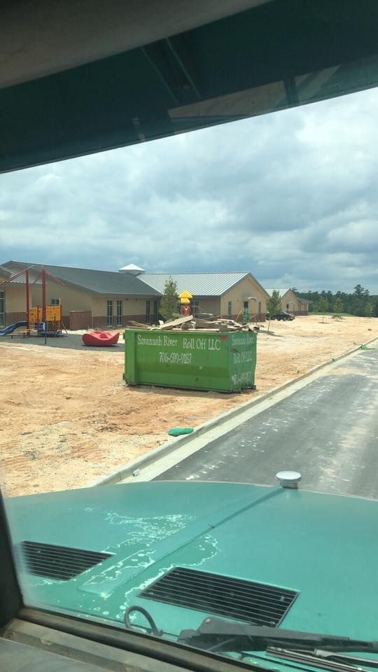 A green dumpster is sitting on the side of the road.